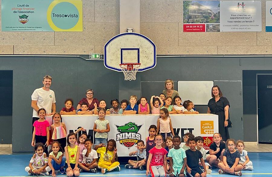 Des enfants et leur coach posent devant un panier de basket pour un événement parrainé par Habitec